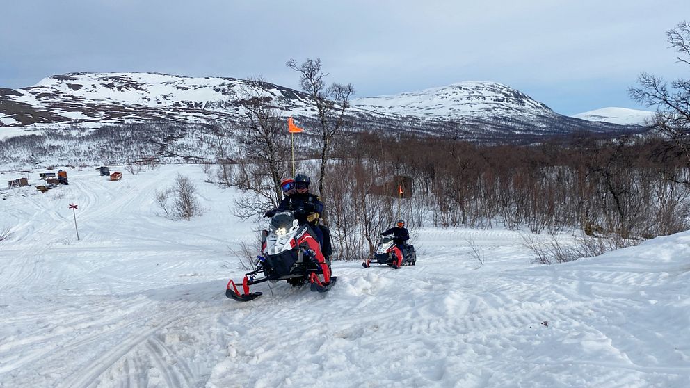 Två röd-vita snöskotrar i fjällmiljö kommer körande mot kameran