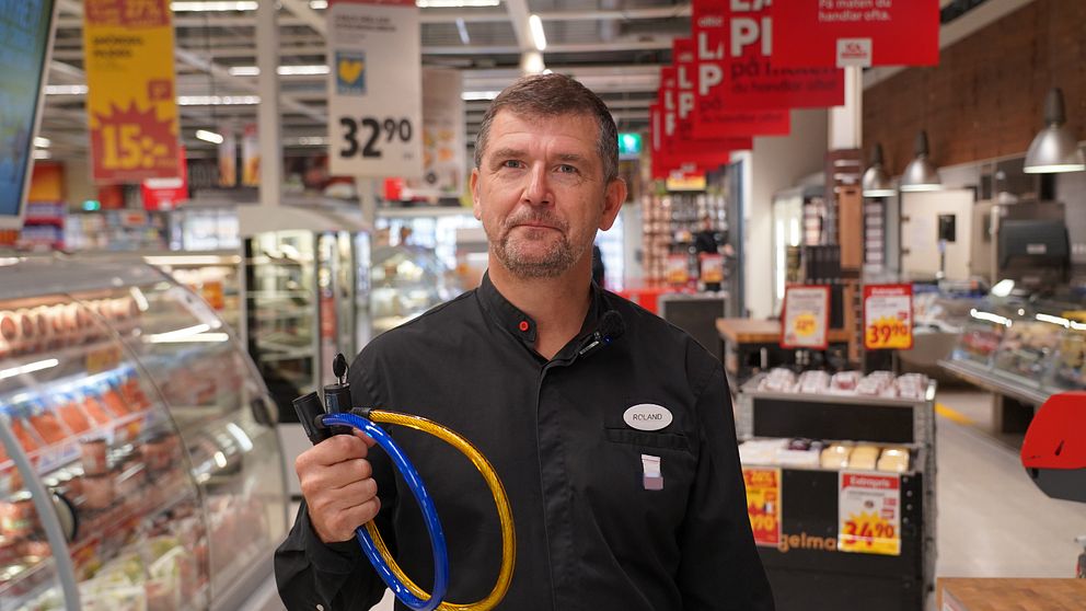 ICA-handlaren står med två lås och tittar in i kameran.