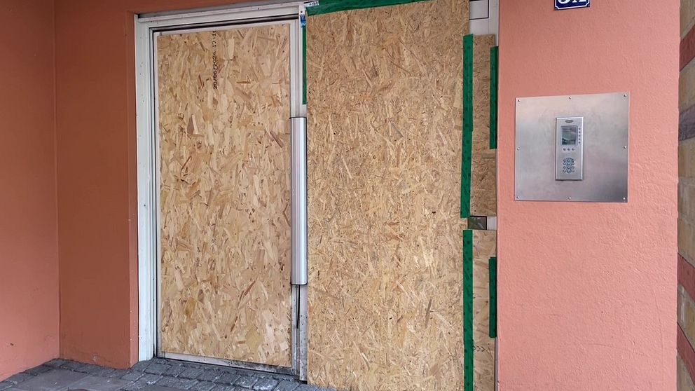 Entrédörr täckt med plywood i renoveringssyfte. På väggen finns en porttelefon.