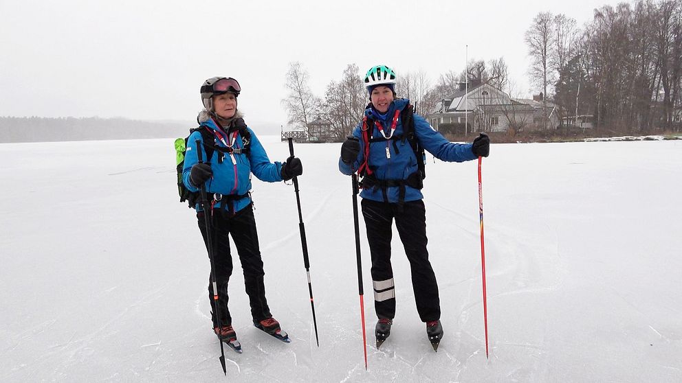 Två kvinnor som står på isen med långfärdsskridskor och utrustning
