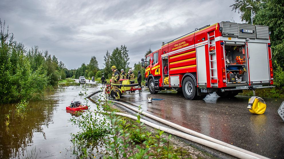 En brandbil står vid en översvämmad å vid en bilväg i Dalarna.