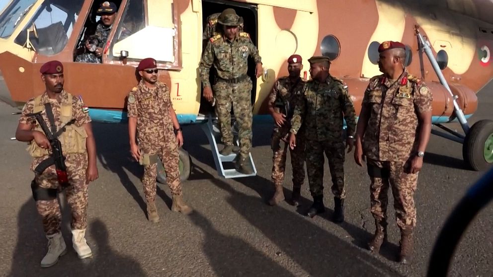 Soldater i camouflage uniform står framför en militärhelikopter.
