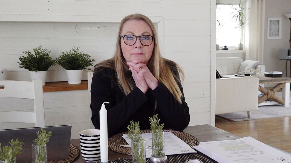 Person vid matbord i ett ljust rum, med dokument och ljus framför sig.