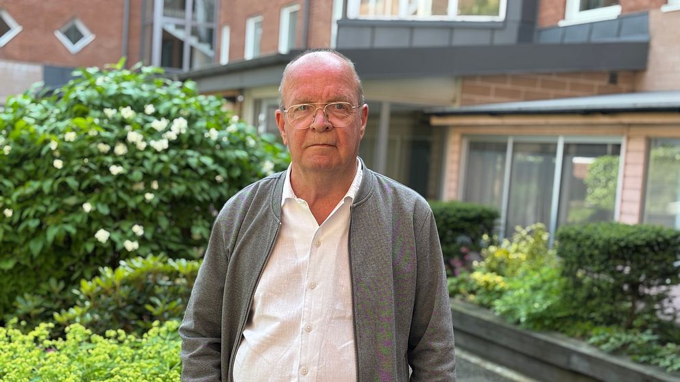 En person står i en grönskande innergård framför bostadshus.