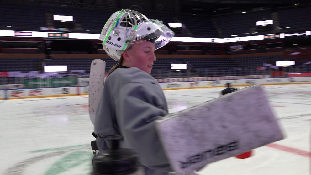 Hockeytjej på is hämtar vattenflaska.