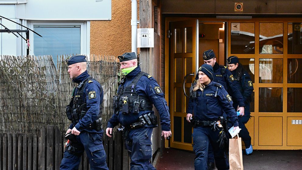 Poliser lämnar en byggnad, en bär en papperspåse.