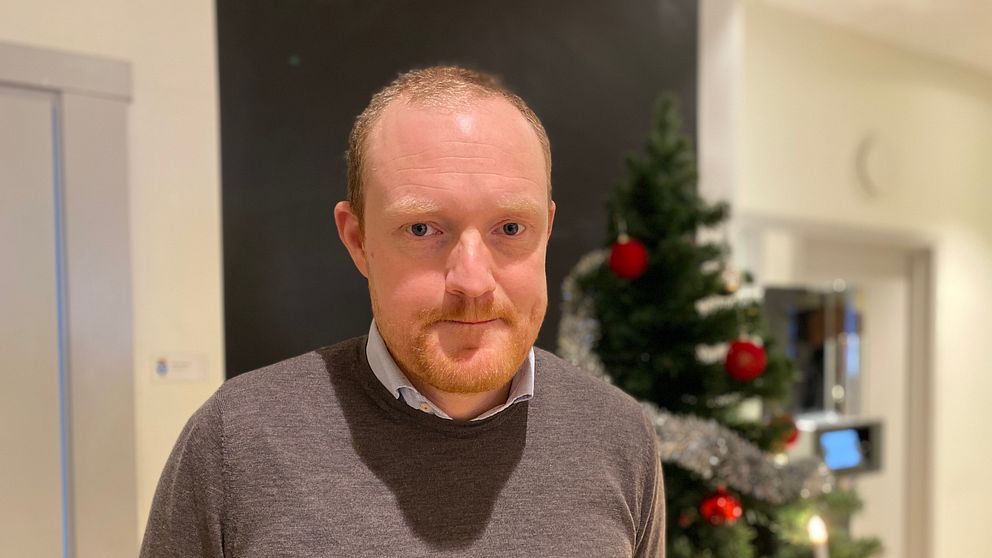 Östersunds kommunstyrelseordförande, Niklas Daoson (S) står framför en julgran dekorerad med röda kulor och silverfärgad girlang, inomhus i en festlig miljö.