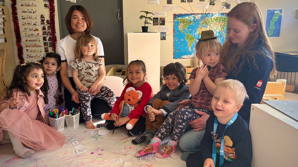 En grupp barn sitter på golvet med leksaker, leksakskarta och pedagog.
