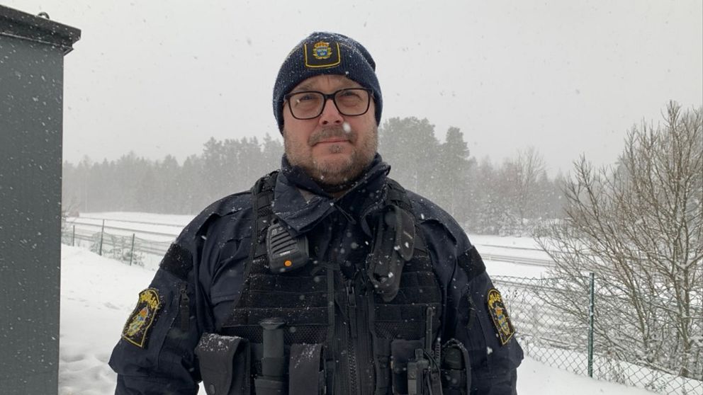 man i polisuniform som står utomhus, snön faller och bakom honom syns en motorväg