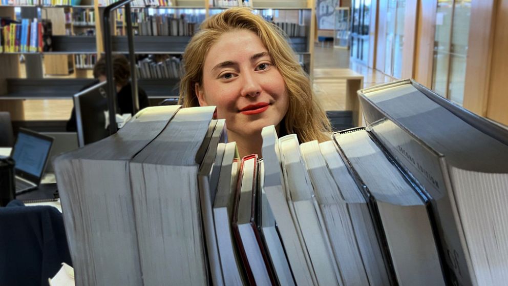 Kvinna med ljust hår bakom böcker i bibliotek, Olivia Rosén vid Karlstads universitet, vinnare av Lilla Psykologipriset 2024