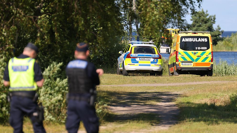 Poliser tittar mot vatten där en polisbil och en ambulans står.