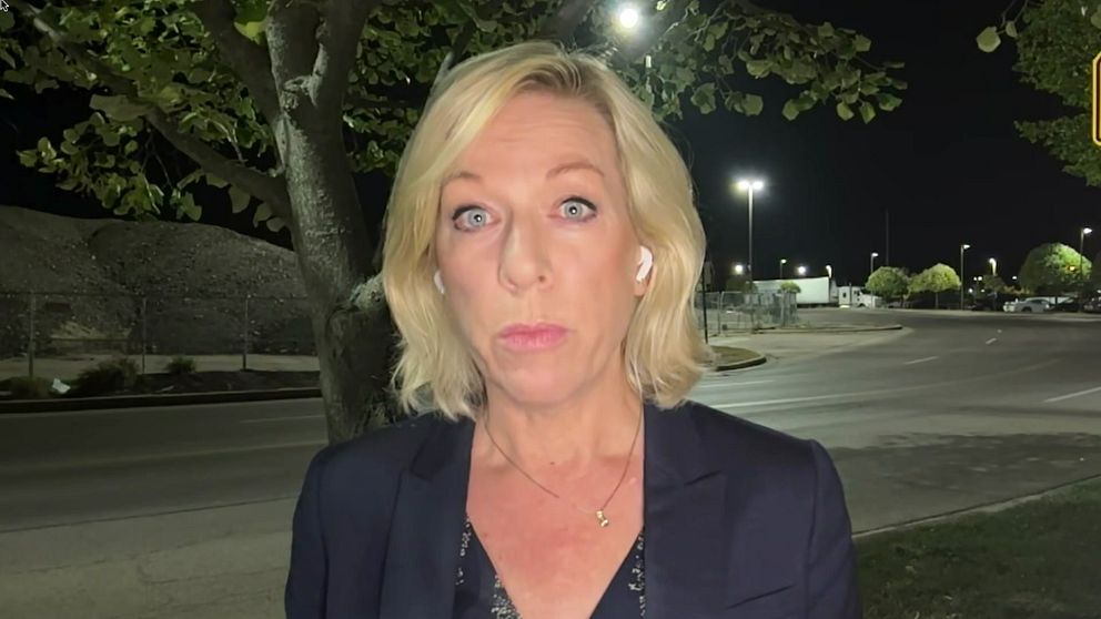 En kvinna (Ginna Lindberg, USA-korrespondent för Sveriges radio) står utomhus i mörker, iförd en mörk blazer. Bakgrunden visar en väg som är svagt upplyst av gatulampor, med träd och en grusig yta i närheten.