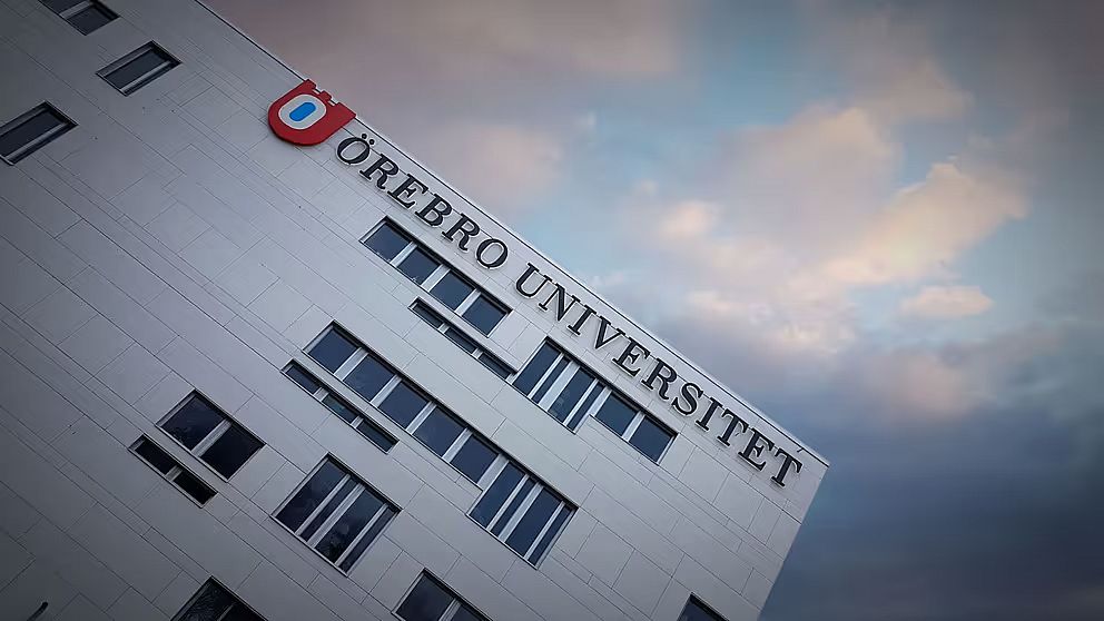 Fasad på Örebro universitet med logotyp och text mot en molnig himmel.
