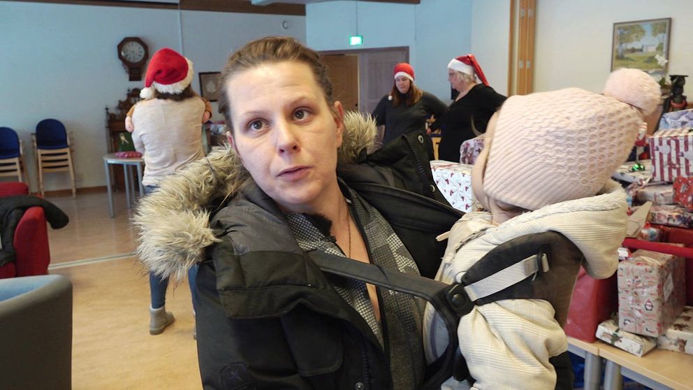 Fyrbarnsmamman Linda i Katrineholm står med barn i famnen framför ett bord med julklappar.