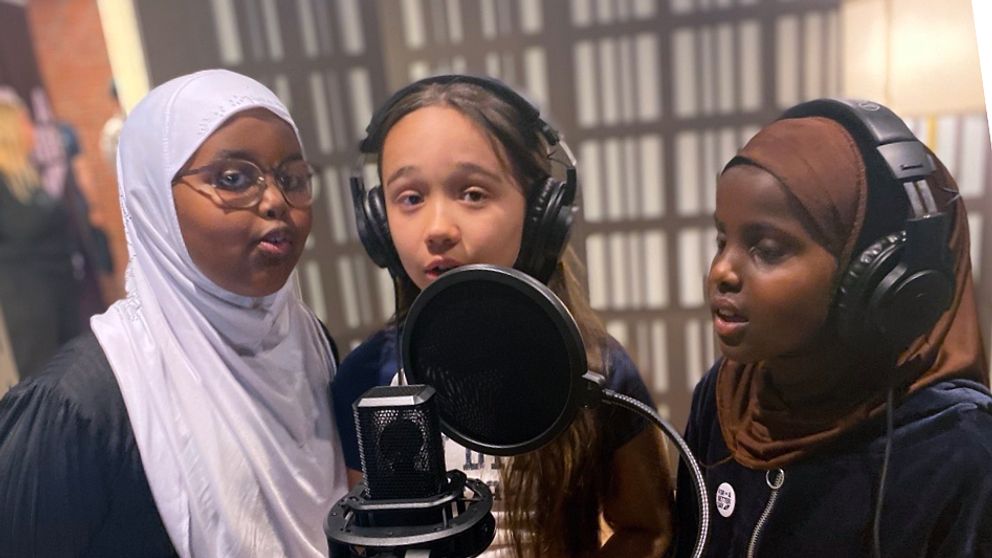 Tre flickor framför mikrofon i musikstudio