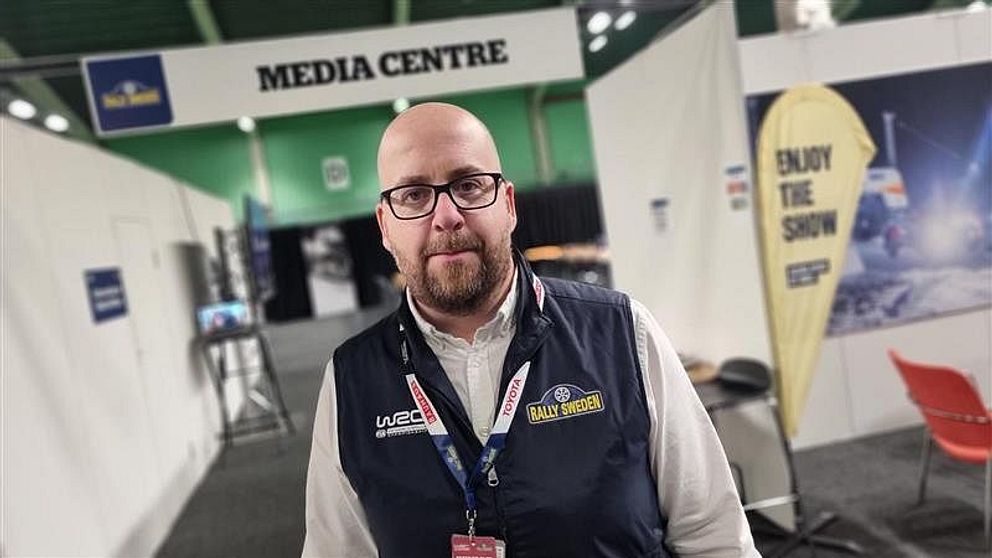 Eric Åström står i en mediecenterlokal med entréskyltar och kontorsmöbler i bakgrunden.