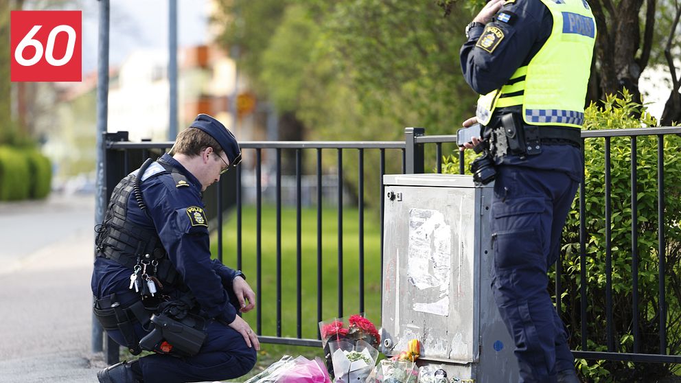 Två poliser vid ett blomhav på trottoaren, minnesplats efter händelse utomhus.
