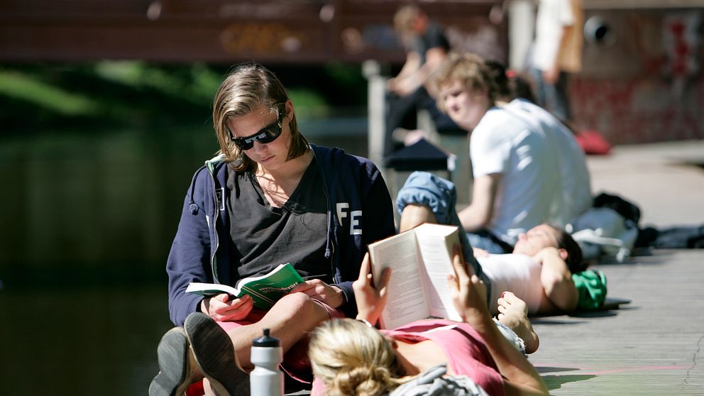 Två kvinnor läser böcker på en brygga i solen.