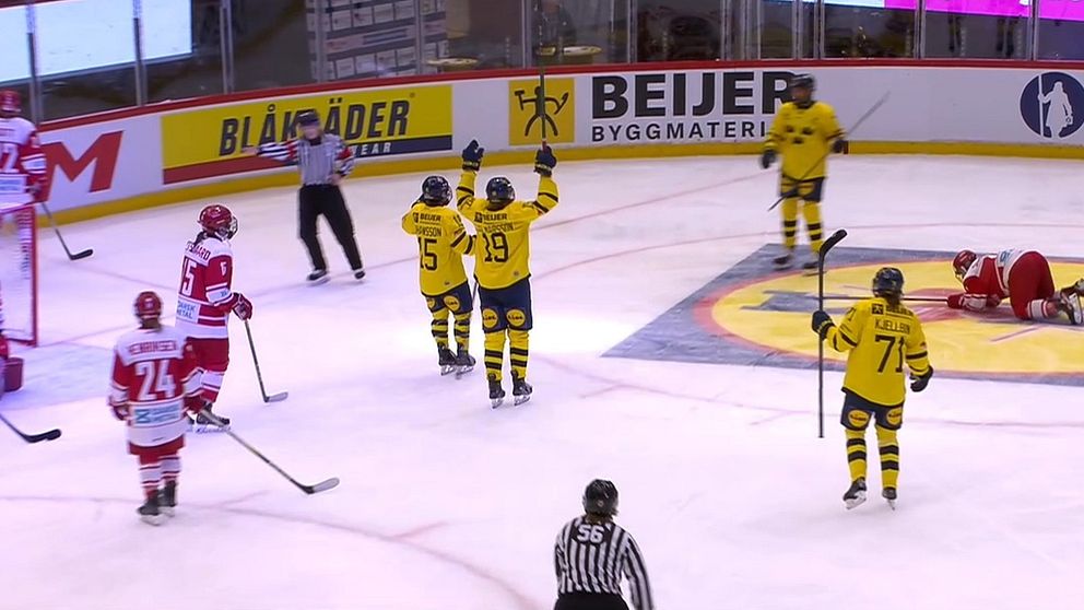 Spelare i gula tröjor jublar efter att ha gjort mål i en ishockeymatch medan spelare i röda tröjor reagerar vid målet och på isen. Domare vakar över spelet på isen.