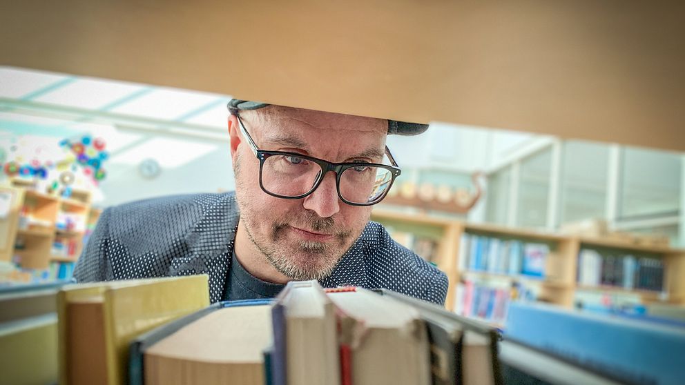 Författaren Per Berg kollar på böcker i en bokhylla.