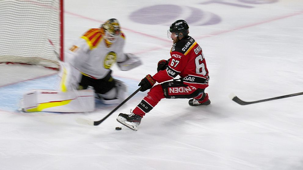 Hockeyspelare i röd tröja utmanar målvakt i vit dräkt under match framför målbur.