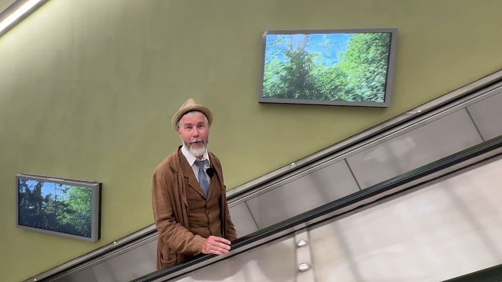 Jan Rydén Bonmot åker rulltrappa i tunnelbana med naturbilder på väggen.