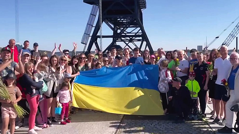 30-tals ukrainare står med den blågula flaggan nere vid den stora lyftkranen i Södra hamn, Luleå.