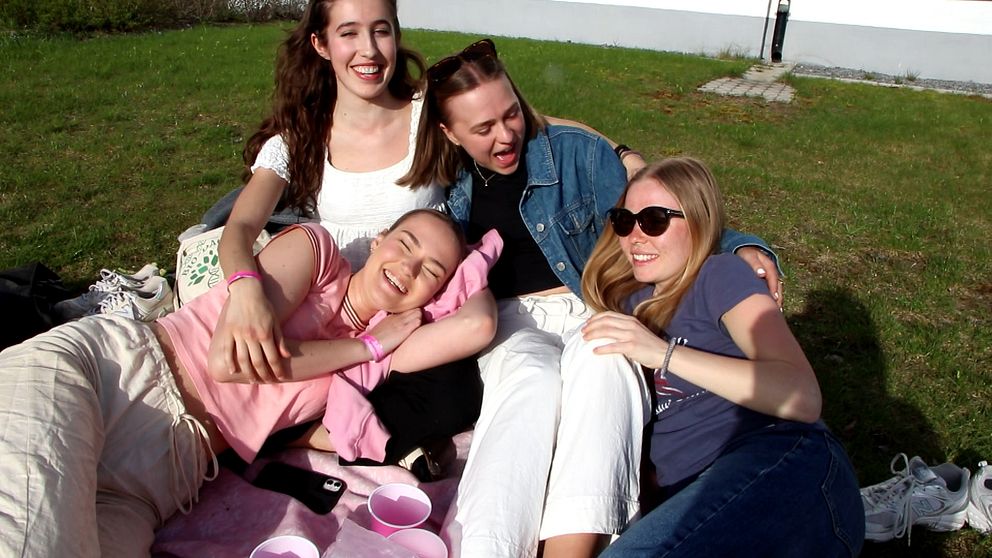 Fyra tjejer sitter på en filt på gräset och skrattar.