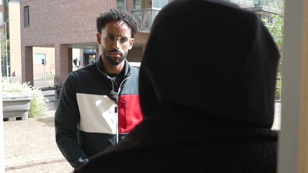 Två personer samtalar utomhus vid en husentré i ett bostadsområde.