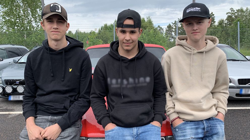 Tre ungdomar sitter på motorhuven på en röd bil.