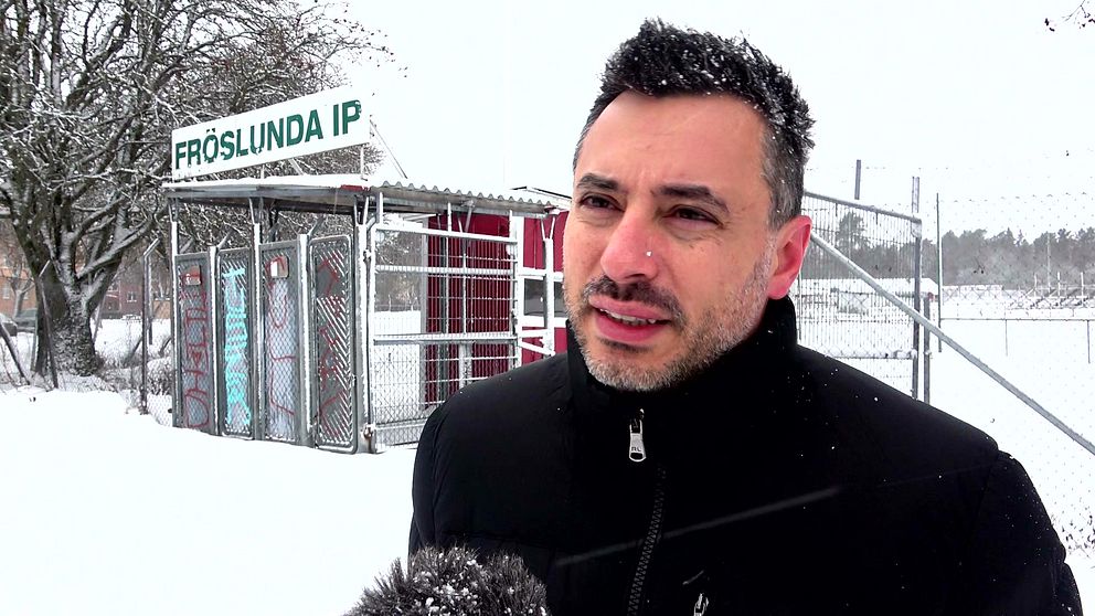 Fredrik Krait står framför Fröslunda IP i snöigt väder, med en fotbollsstadion och byggnad i bakgrunden.