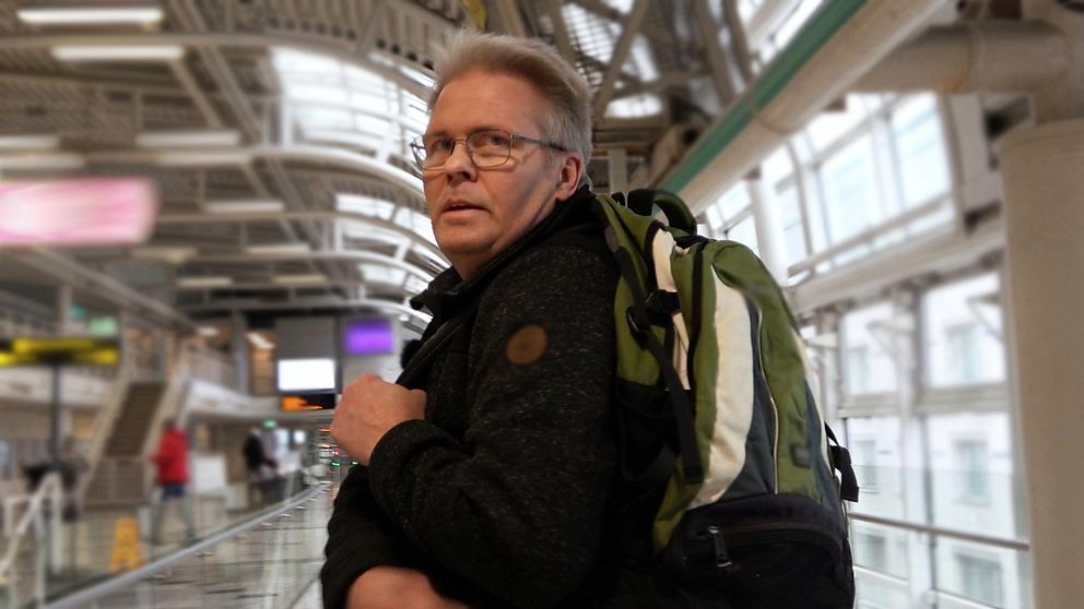 en man med en ryggsäck står på en tågstation och tittar mot kameran