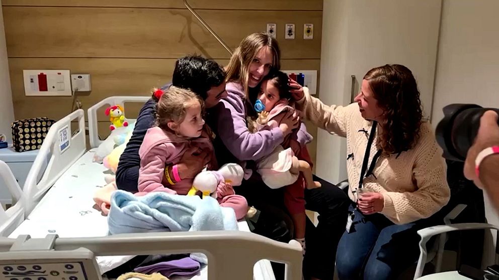 Familj sitter på sjukhussäng, föräldrar kramar om sina döttrar.