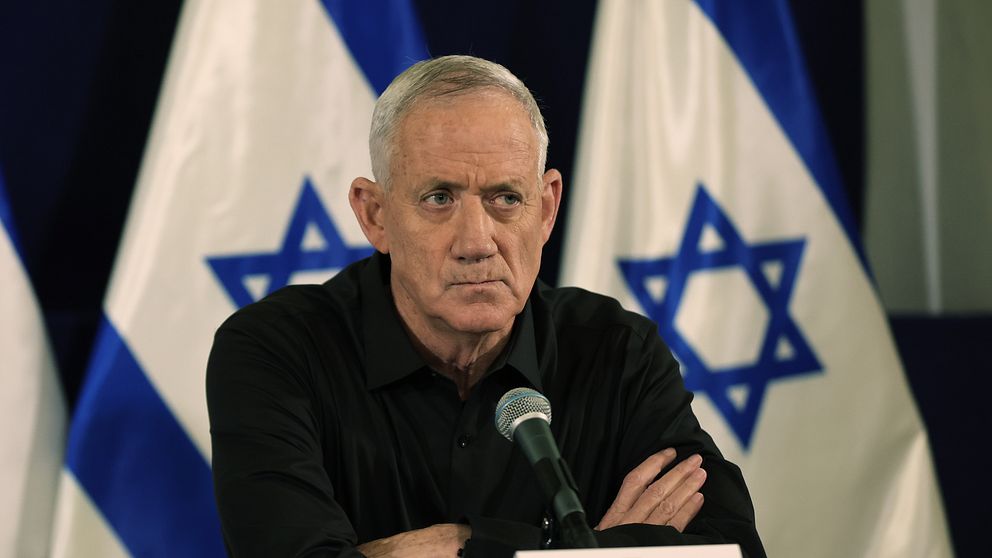 Benny Gantz i svart skjorta framför två israeliska flaggor