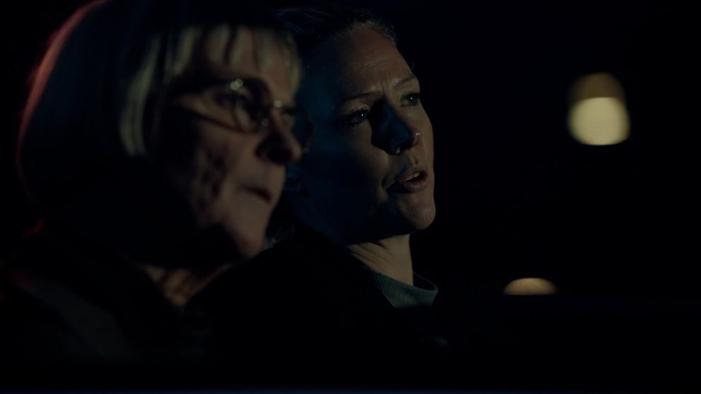 Två kvinnor sitter i en bil i mörkret och spanar ut