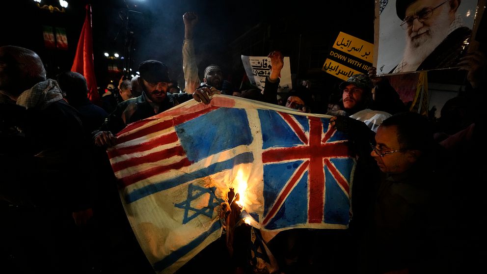 En grupp män sätter eld på en bit tyg eller papper som föreställer USA:s, Israels och Storbritanniens flaggor.
