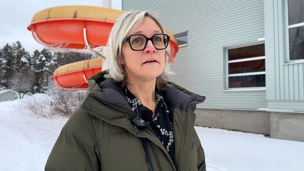 Åsa Säfsten Boman, verksamhetschef för bad i Umeå, i en mörk vinterjacka står utanför badhuset Storsjöhallen i Holmsund. Badhuset med röda rutschkanor i bakgrunden, omgiven av snötäckta omgivningar.
