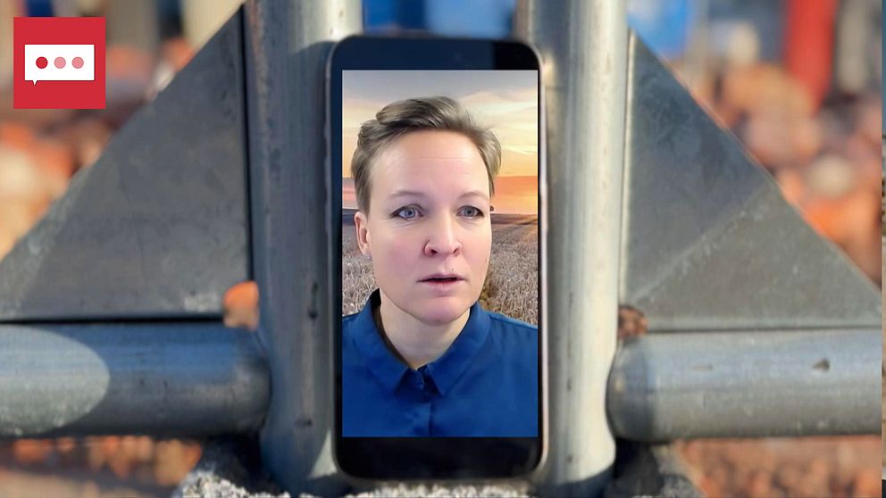 En mobiltelefon är placerad mellan två metallstänger med en bakgrund som visar en landskapsvy vid solnedgång. Mobilskärmen visar en person i blåt tröja, omgiven av en oskarp, urban miljö. Bilderna och omgivningen ger en känsla av modern kommunikation i en industriell setting.