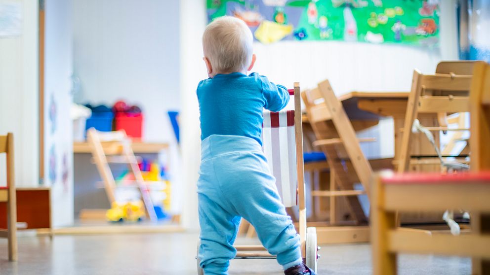 Ett litet barn som går bakom en leksaksvagn i en ljus och färgglad förskolemiljö.