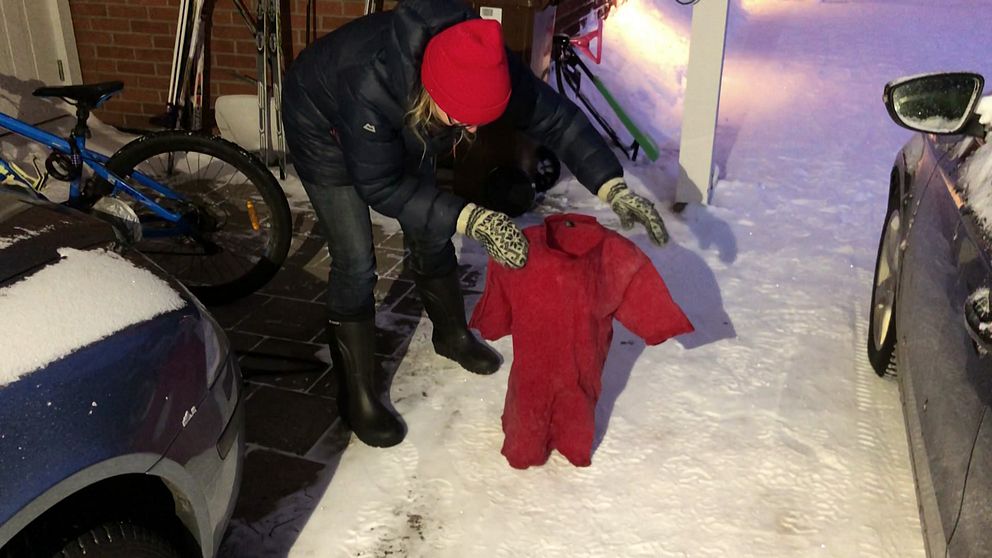 en kvinna i dunjacka och mössa ställer en t-shirt som är stelfrusen, på den snöiga marken