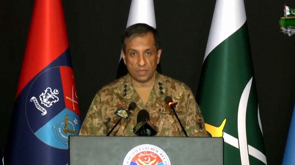 Pakistansk militärperson talar vid podium med flera flaggor i bakgrunden och urdu-text längst ner.