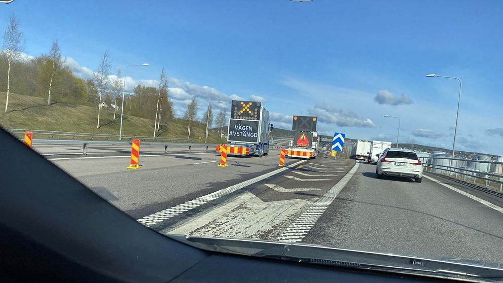 Vägavstängning med varningsskyltar och bilar som sakta kör förbi vägarbete.