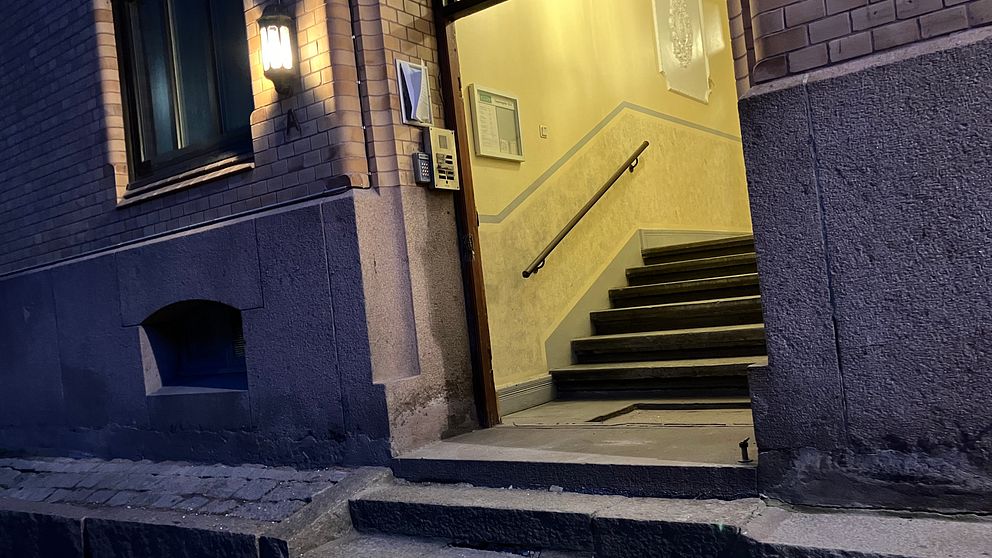 Entré till en byggnad med upplyst trapphuset på kvällstid. Trappor leder in till dörren.