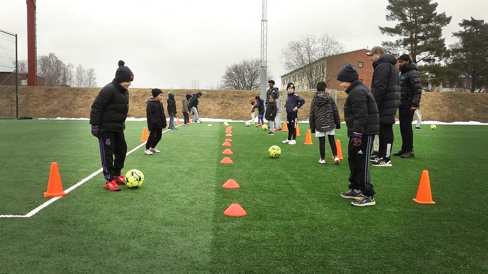 Barn på en fotbollsplan med koner och fotbollar.