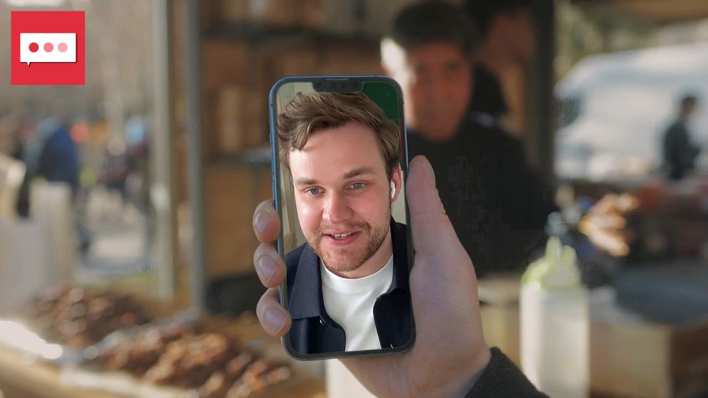 En person håller upp en mobiltelefon vid ett café.