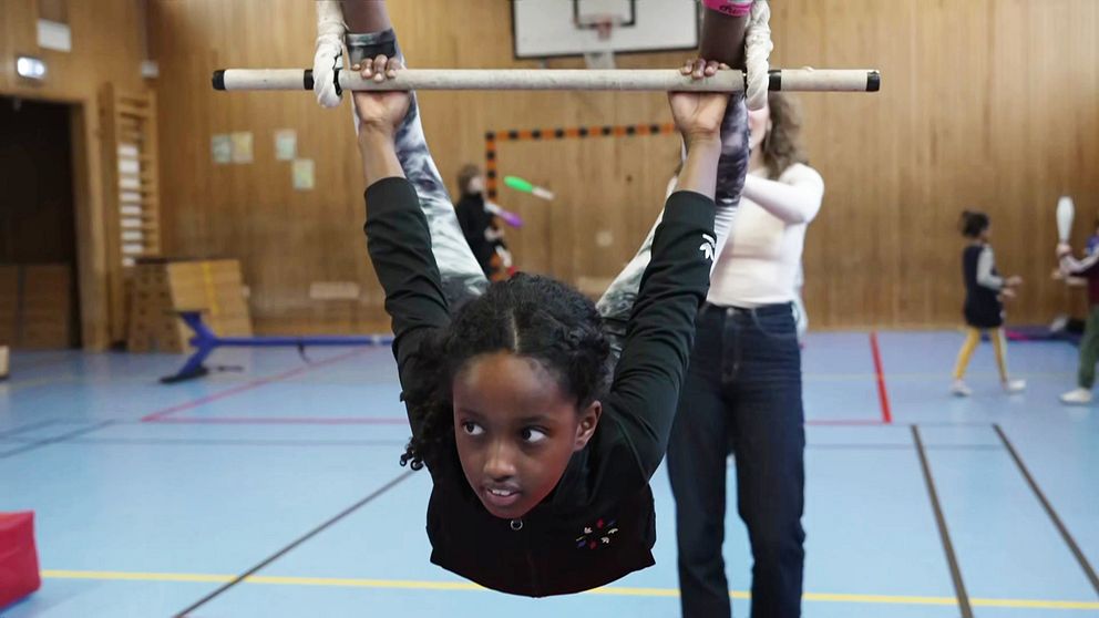 Barn tränar gymnastik med handledares hjälp i en gymnastiksal.