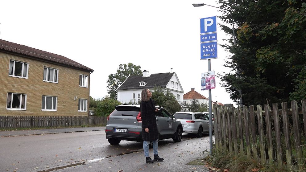 SVT reporter står och tittar på parkeringsavgiftsskylten
