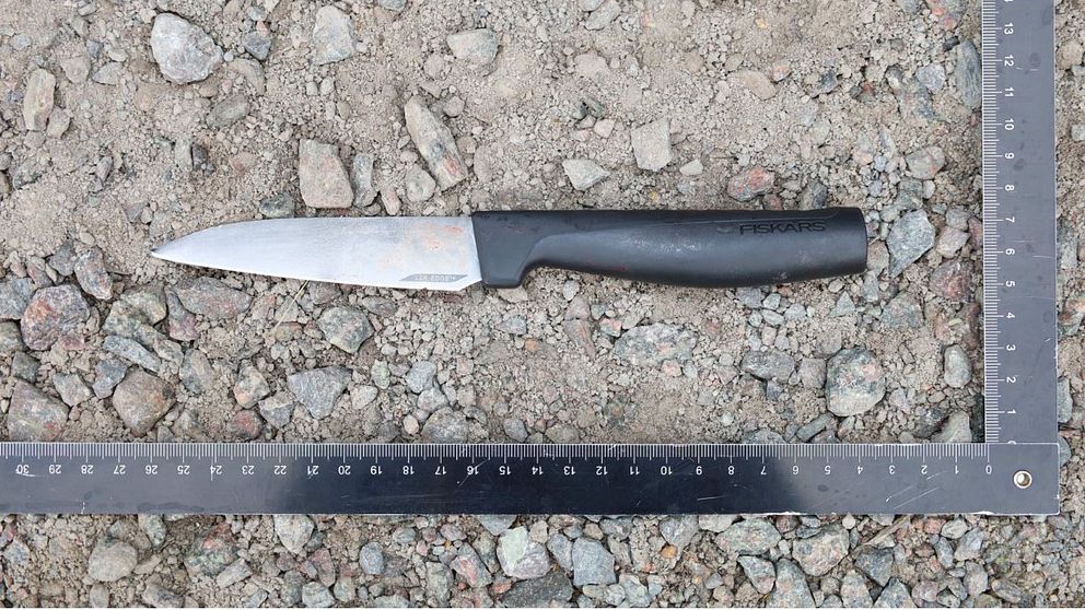 Kniv ligger på en grusig markomgivning inom ett mätverktyg i vinkel, vilket används för att bedöma knivens storlek i ett kriminaltekniskt sammanhang.