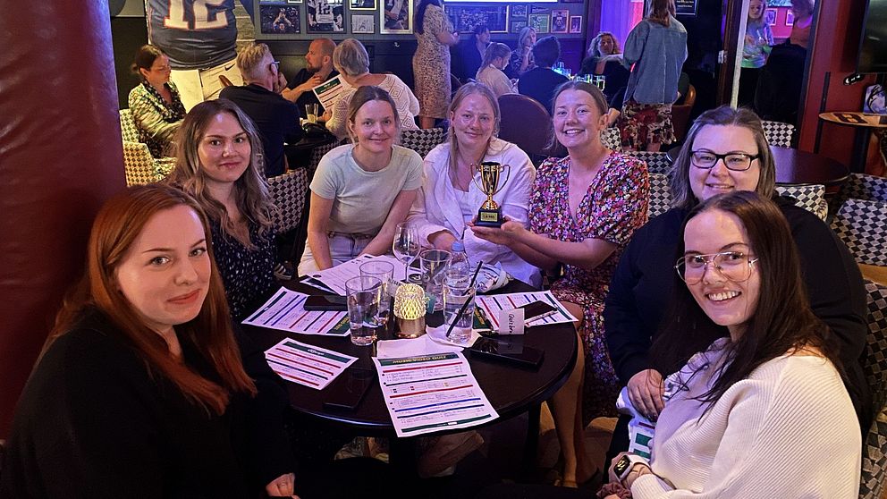 Flera personer sitter vid ett bord på en sportbar, en kvinna håller i en pokal.