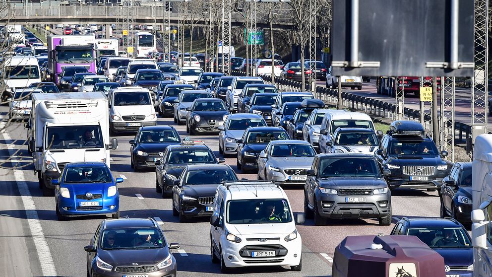 Tät trafik på flerfilig motorväg under en klar dag. Bilar och lastbilar kör i köbildning.